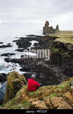 Londrangar thufubjarg Klippen und Meer Stacks. Tourist guy sitzt auf einem Felsen und blickt auf das Meer. Berühmte Touristenattraktionen Islands Stockfoto