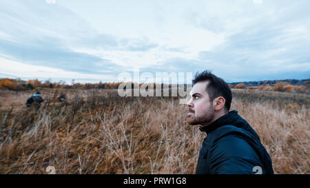 Mann mit einem Manischen Ausdruck in Schwarz Jacke stalking Opfer in den Wald. Konzept der Herbst Verschlimmerung in psychisch kranke Menschen. Stockfoto