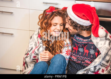 Glückliches junges Paar in Santa Hut und Geweih Stirnband umarmen und sitzen zusammen im neuen Haus Stockfoto