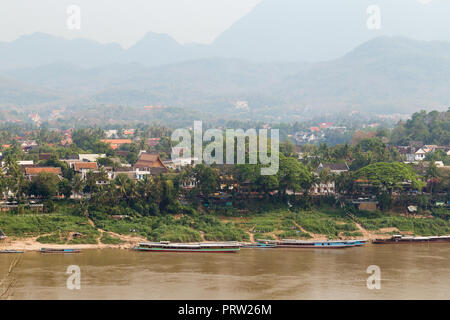 Angelegte Boote auf dem Mekong Fluss, Stadt Luang Prabang und die Berge im Hintergrund gesehen vom Chomphet Bezirk an einem sonnigen Tag in Laos. Stockfoto