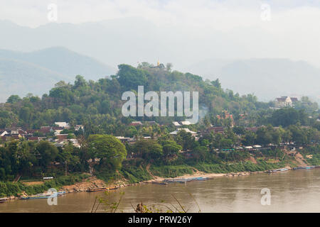 Angelegte Boote auf dem Mekong Fluss, Stadt Luang Prabang, Mount Phousi (Phou Si, Phusi, Phu Si) und Berge im Hintergrund in Luang Prabang, Laos. Stockfoto