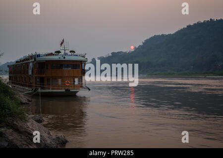 Ansicht eines günstig Kreuzfahrt Schiff auf dem Mekong und Chomphet Bezirk über den Fluss in Luang Prabang, Laos, bei Sonnenuntergang. Stockfoto