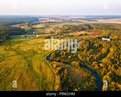 Herbst ländlichen Luftaufnahme mit Wiese, Fluss, Dorf, unbefestigte Straße und Landwirtschaft Felder im Hintergrund. Sonnenuntergang Herbst Szene von oben Stockfoto