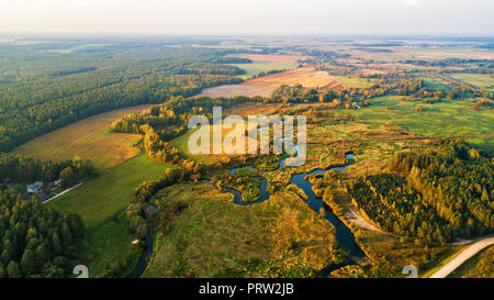 Herbst ländlichen Luftaufnahme mit Wiese, Fluss, Dorf, unbefestigte Straße und Landwirtschaft Felder im Hintergrund. Sonnenuntergang Herbst Szene von oben Stockfoto