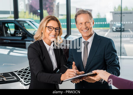 Happy business Paar Unterzeichnung Papiere für den Kauf neuer Wagen im Showroom Stockfoto