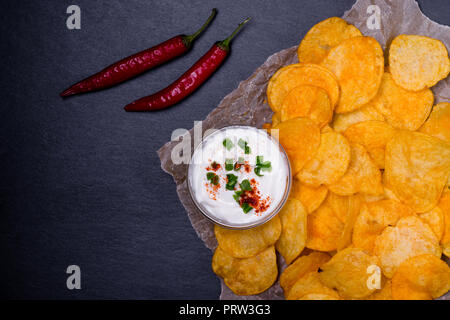 Chips mit Dip und Peperoni auf Pergamentpapier. Auf dunklen schwarzen Steintisch Hintergrund. Ansicht von oben. Stockfoto