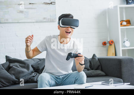 Glückliche junge Mann in virtual reality Headset spielt mit Joystick zu Hause Stockfoto