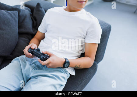 Zugeschnittenes Bild von asiatischer Mann spielen video game und liegend auf dem Sofa zu Hause Stockfoto