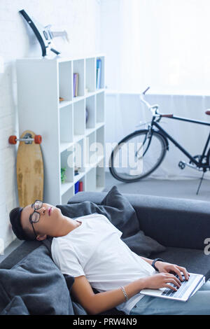 Hohe Betrachtungswinkel von Stattlichen asiatischer Mann schlafen und Holding Laptop auf dem Sofa zu Hause Stockfoto