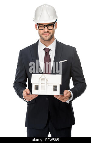 Selbstbewussten jungen männlichen Architekt in harten Hut mit Miniatur Haus isoliert auf weiss Stockfoto