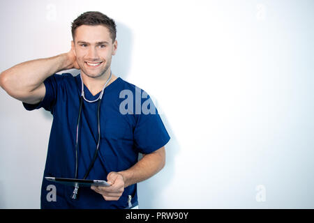 Stattliche männliche Arzt oder Krankenschwester in blau Scrubs, Holding digital Tablet und lächelnd, während bei Camera suchen Stockfoto