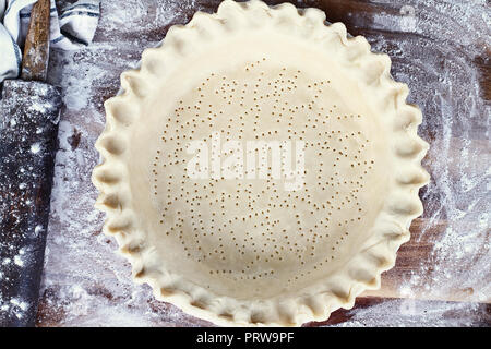 Hausgemachte butter Pie Crust in Pie Platte mit geriffelten Rand gequetscht, nudelholz und extra Ball von Teig über Bemehlten rustikalen Holzmöbeln Hintergrund. Kruste ist Stockfoto