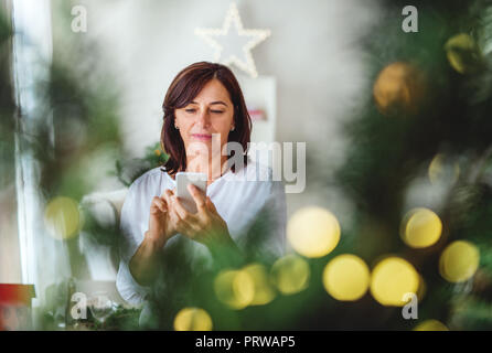 Eine ältere Frau mit Smartphone an Weihnachten zu Hause. Kopieren Sie Platz. Stockfoto