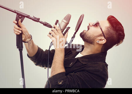 Begabte junge Mann mit dem braunen Fell und Gläser ein Lied singen im Studio Aufnahme Stockfoto