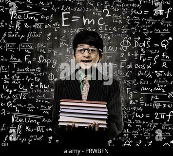 Intelligente Cute Little Boy Holding Buch und Brille vor einem Schwarzen Brett, chemische Formeln an Bord geschrieben werden Stockfoto