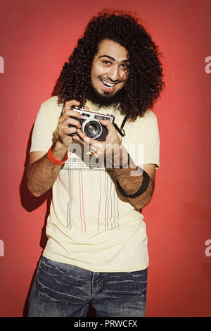 Nahaufnahme von einem stattlichen leidenschaftlich expressive cool Junge brünette Fotografin Männer mit langen Locken mit einem Vintage Spiegelreflexkamera stehend gegen Stockfoto