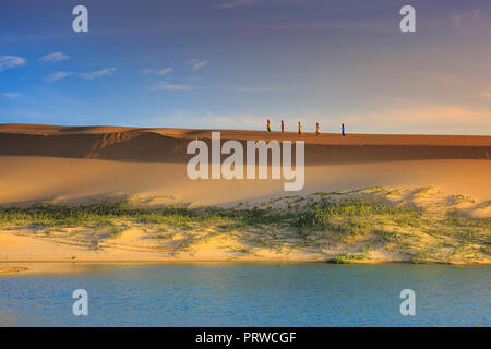 Cham Frauen in traditioneller Kleidung gehen über Sanddünen zu Sammeln von Wasser in der Nähe von Phan Rang, Vietnam. Viele Leute halten Cham Stockfoto