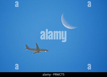 CHARLOTTE, NC (USA) - Oktober 4, 2018: ein Verkehrsflugzeug in niedriger Höhe unter ein Halbmond bei Sonnenaufgang. Stockfoto