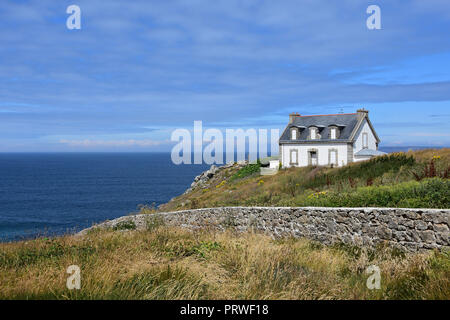 Sonniger Tag am Kap Pointe du Millier, Bretagne, Frankreich. Von der Sonne angezündet altes weißes Haus hoch auf grünem Hügel, bedeckt mit wilden Kräutern. Blauer Ozean dahinter Stockfoto