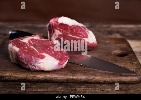 Zwei Rohmaterial Rib-Eye-Steaks mit Messer auf Holz- Hintergrund Stockfoto