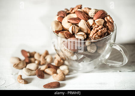 Verschiedene Nüsse in eine schöne transparente Schale auf Holz Hintergrund, Konzept der gesunden Ernährung Stockfoto