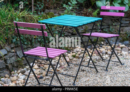 Zwei rosa hölzerne Klappstühle und einen blauen Tabelle stehen auf Kies im Hinterhof eines Cafe in natürlichem Licht am Abend Stockfoto