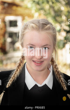 Elf Jahre alte Mädchen mit blonden Zöpfen vor Französisch Windows posing und beleuchtet nach Prallte Flash mit einem Garten hinter Stockfoto