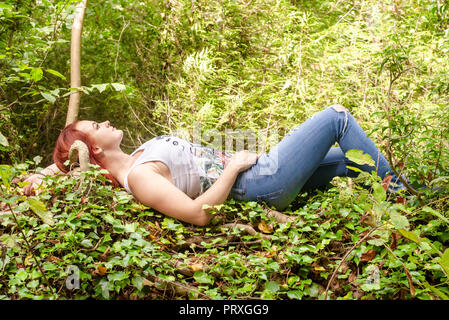 Rothaarige junge Frau liegt im Wald Stockfoto