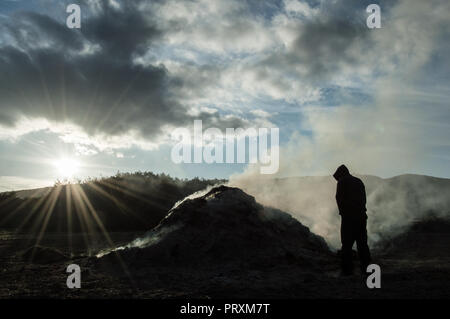 Eine vermummte Gestalt, gegen die weißen Rauch von einem Lagerfeuer. Von der Sonne beleuchtet. Stockfoto