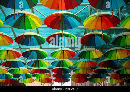 Bunte Anzeige der offenen regenbogenfarbenen Sonnenschirmen im Freien in Straße unter blauen Markise an einem sonnigen Tag. Stockfoto