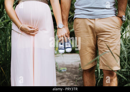 Den mittleren Abschnitt Foto der schwangeren Frau und ihrem Mann die kleine Baby Schuhe Stockfoto