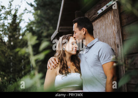 Mann, ist das Küssen seine schwangere Frau auf ihrer Stirn und sie lächelt Stockfoto