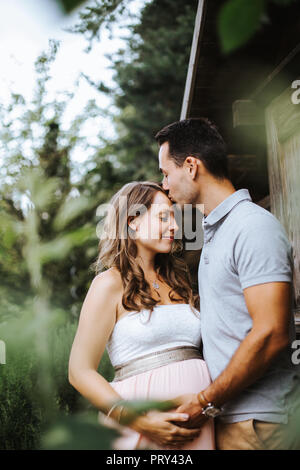 Mann, ist das Küssen seine schwangere Frau auf ihrer Stirn und sie lächelt Stockfoto