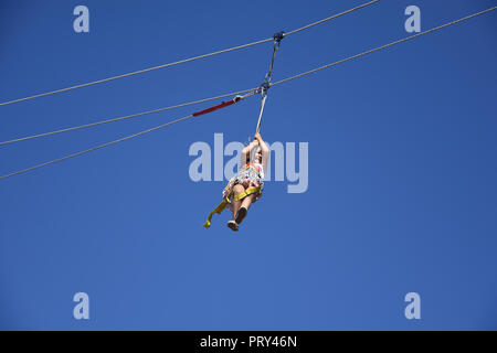 Glücklich lächelnd kleine Mädchen hängen auf einer zip-line hoch in den blauen Himmel während der Extreme Sports Festival Herbst in Sofia, Bulgarien 2018 Stockfoto