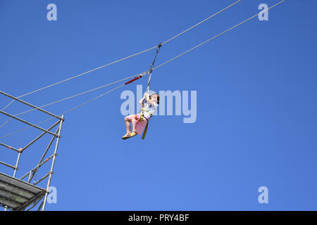 Glücklich lächelnd kleine Mädchen hängen auf einer zip-line hoch in den blauen Himmel während der Extreme Sports Festival Herbst in Sofia, Bulgarien 2018 Stockfoto