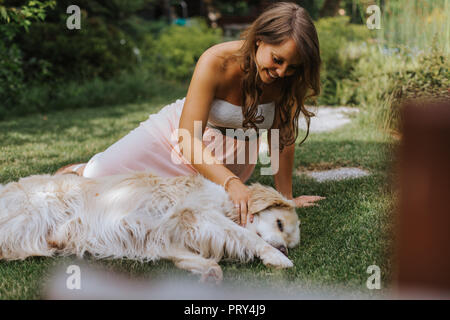 Schwangere Frau saß auf dem Gras und spielt mit Golden Retriever Stockfoto