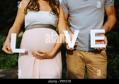 Schwangere Frau und ihr Mann sind die Buchstaben für die Liebe in ihren Händen mit 'o' wird Ihr Bauch Stockfoto