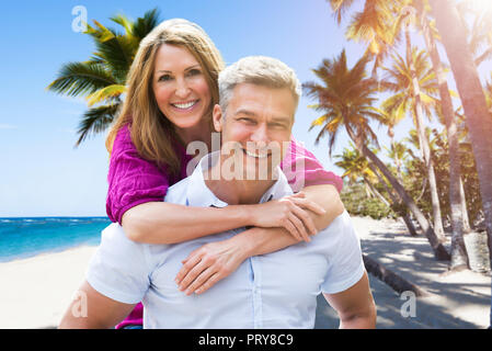 Porträt eines lächelnden reifer Mann, Huckepack zu seiner Frau am Strand Stockfoto