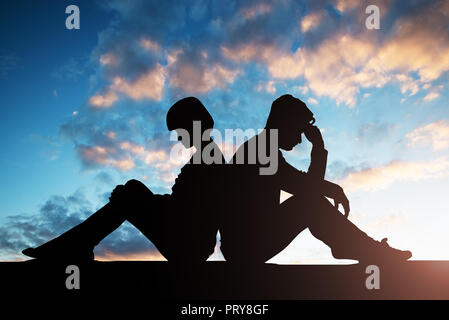 Silhouette von Sad Paar Rücken an Rücken sitzend Gegen bewölkter Himmel Stockfoto