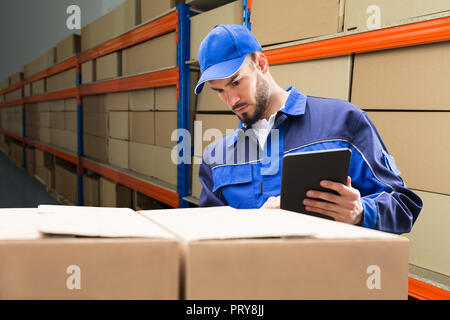 Junge Lieferung Mann in Uniform Kontrolle sein Paket auf digitalen Tablet Stockfoto