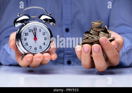 Close-up In eines Mannes Hand, Wecker und goldenen Münzen Stockfoto