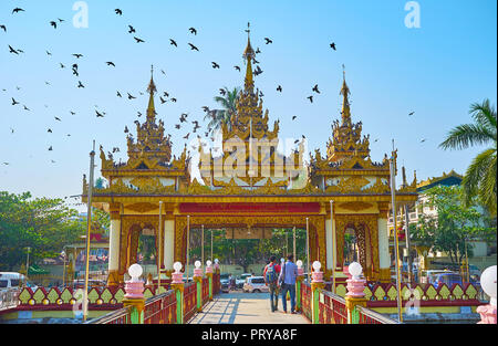 YANGON, MYANMAR - Februar 27, 2018: Der Ausblick vom Gericht Kyay Thone Pagode mit Teichen und Brücken auf Herde von Tauben, fliegen über den entranc Stockfoto