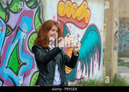 Rothaarige Mädchen, junge Frau in Leder Jacke eine selfie mit Ihrem Smartphone vor Graffiti, in der Nähe von Finale Ligure Stockfoto