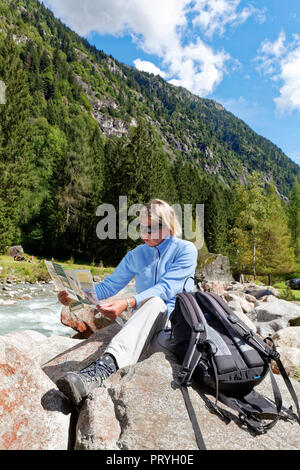 Weibliche Wanderer mit Rucksack liest Wanderkarte am Fluss Sarca, Val Genova, Genova Tal, in der Nähe von Carisolo Stockfoto