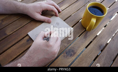 'Business'-nachdenklichen Mann Skizzen ein Mann in Anzug und Krawatte auf eine Serviette, während er trinkt eine Tasse Kaffee. Stockfoto