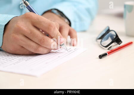 Mann mit Stift in der Hand. Gläser, Bleistift und OME-Blatt auf den Tisch. Stockfoto