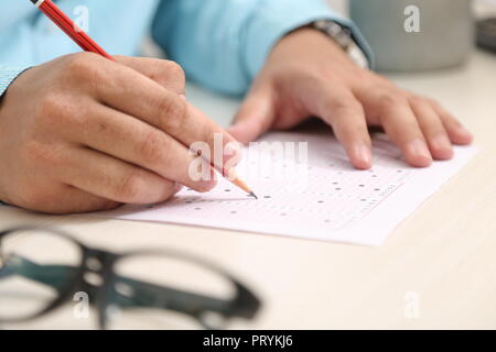 Bild von Mann füllt OME-Blatt mit Bleistift. Portrait von Gläsern auf dem Tisch. Stockfoto