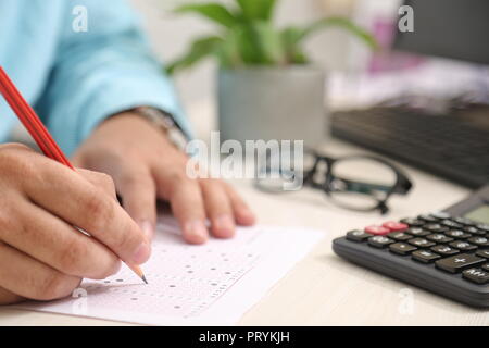 Bild von Mann füllt OME-Blatt mit Bleistift. Portrait von Brille, Rechner, Tastatur und Blumentopf auf dem Tisch. Stockfoto