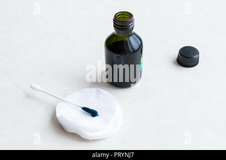 Ein Mann verwendet ein grünes Antiseptikum, hält einen Wattestäbchen in den Händen. Zelenka in einer Flasche. Stockfoto