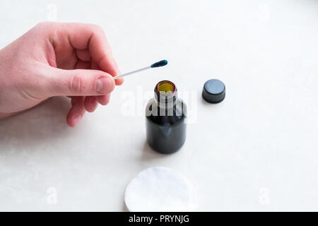 Ein Mann verwendet ein grünes Antiseptikum, hält einen Wattestäbchen in den Händen. Zelenka in einer Flasche. Stockfoto